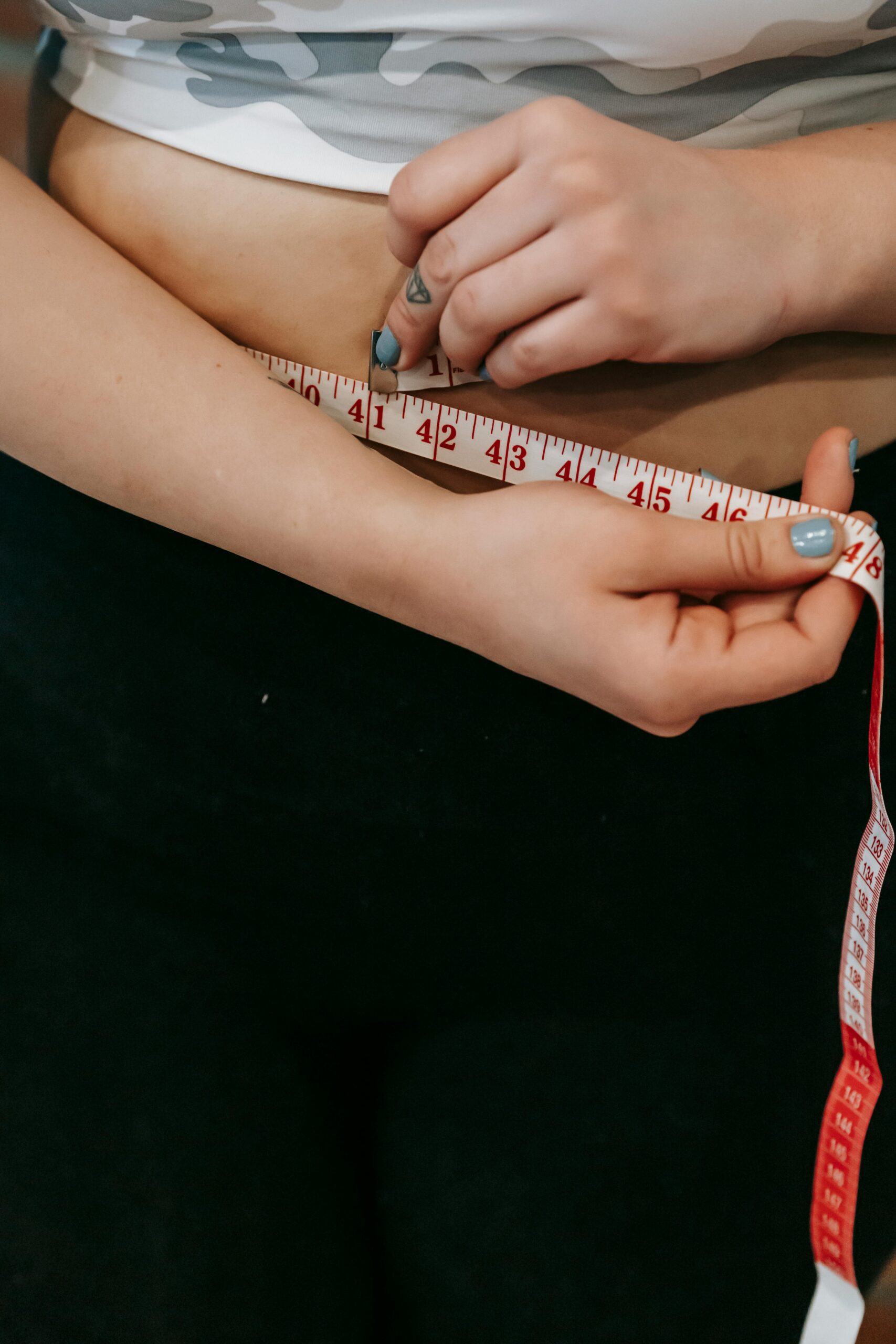 High angle of crop faceless overweight female measuring waist with centimeter for weight loss