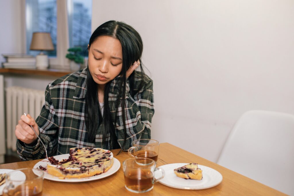 Zespól Jelita Drażliwego (IBS), wzdęcia i Oś Jelitowo-Mózgową Woman in plaid shirt thoughtfully eats blueberry pie in a cozy indoor setting.
