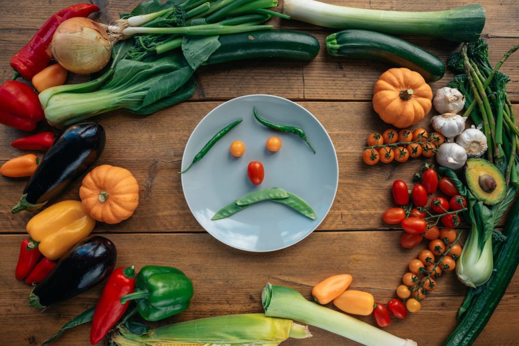 Insulinooporność to nie wyrok. Jak odzyskać energię i schudnąć bez restrykcji? Playful vegetable arrangement creating a sad face on a plate surrounded by fresh produce.